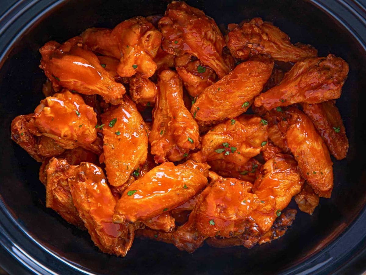 Cooked buffalo wings in slow cooker insert.