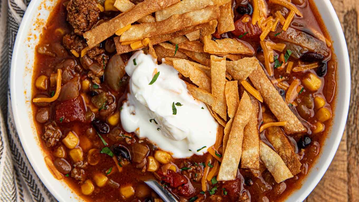 Taco Soup in bowl with sour cream and cheddar cheese with spoon