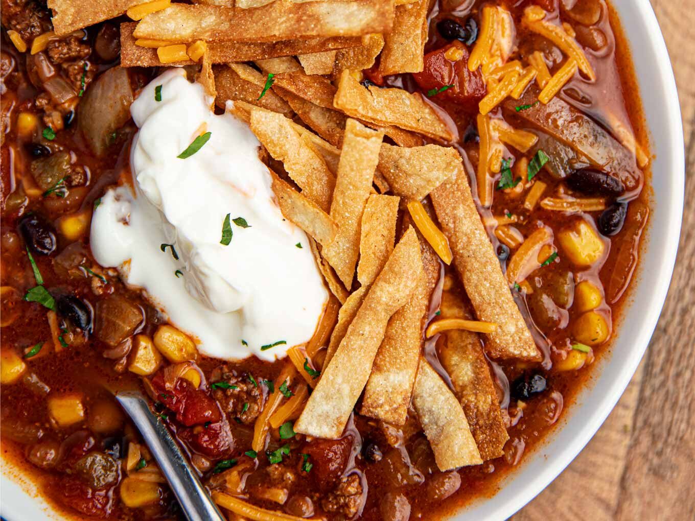 Bowl of Ground Beef Taco Soup made in slow cooker in a white bowl with sour cream and cheese and chips