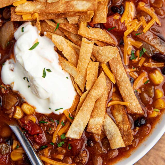 Bowl of Ground Beef Taco Soup in a white bowl with sour cream and cheese and chips