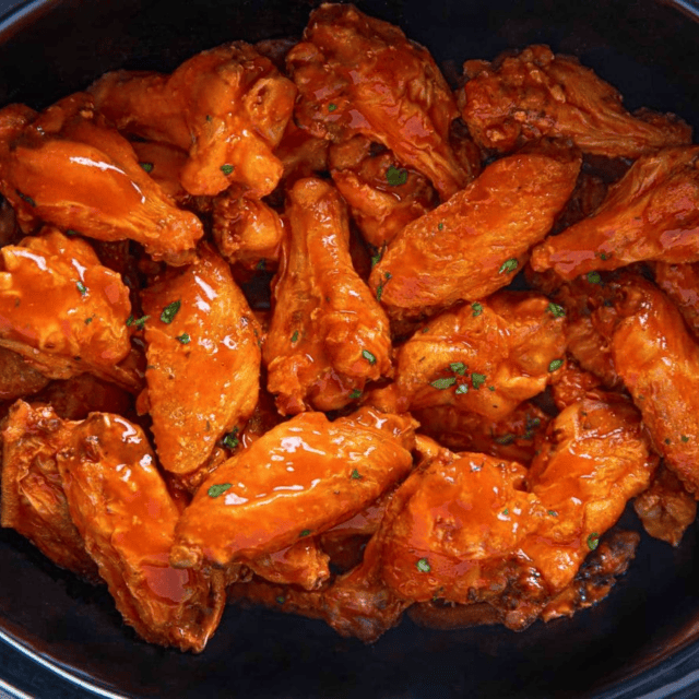 Cooked buffalo wings in a slow cooker insert.