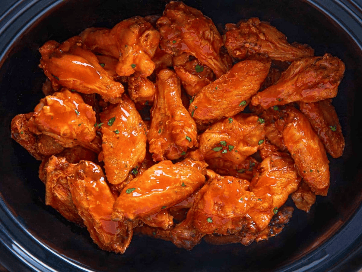 Cooked buffalo wings in a slow cooker insert.