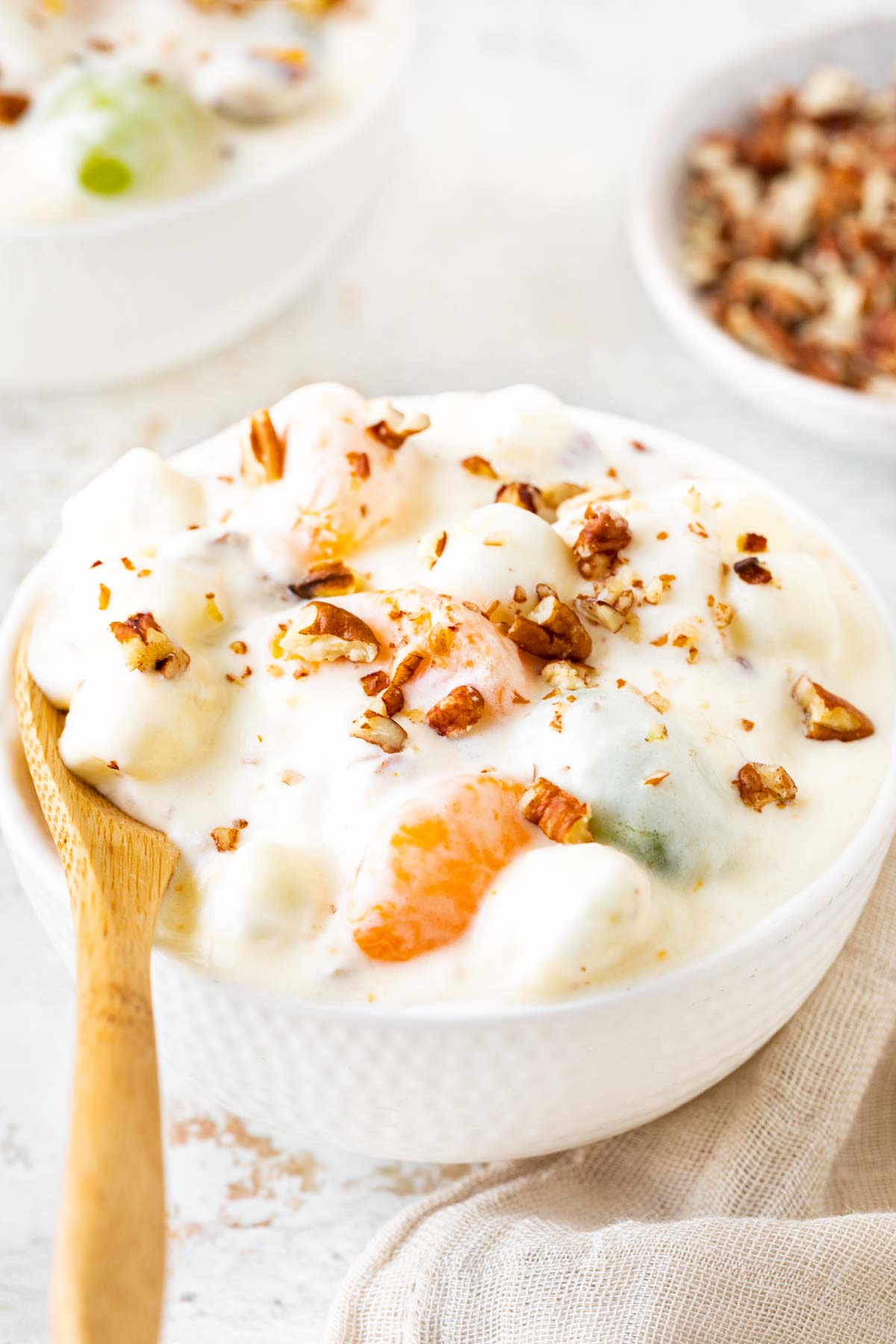Overnight Fruit Salad with whipped cream and nuts in bowl with spoon