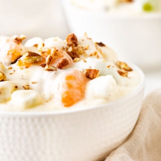 Overnight Fruit Salad with whipped cream and nuts in bowl