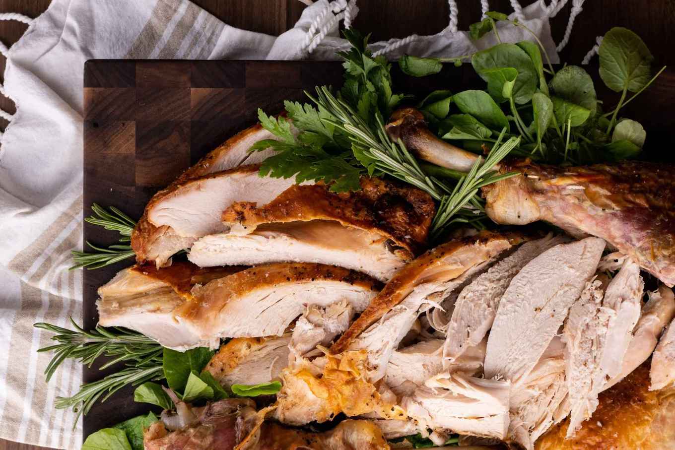 Roaster Oven Turkey sliced on cutting board with fresh herbs
