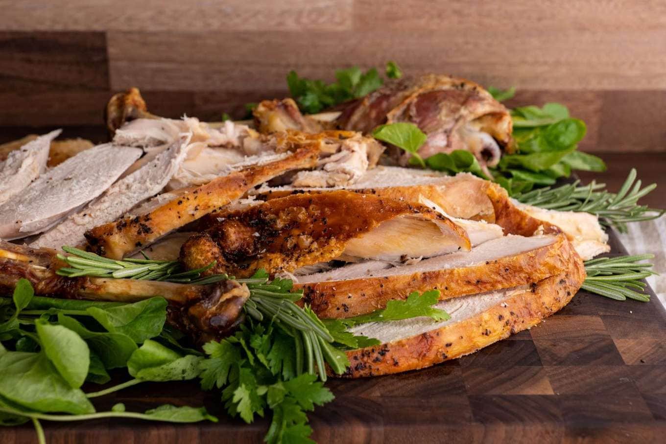 Roaster Oven Turkey sliced on cutting board with fresh herbs