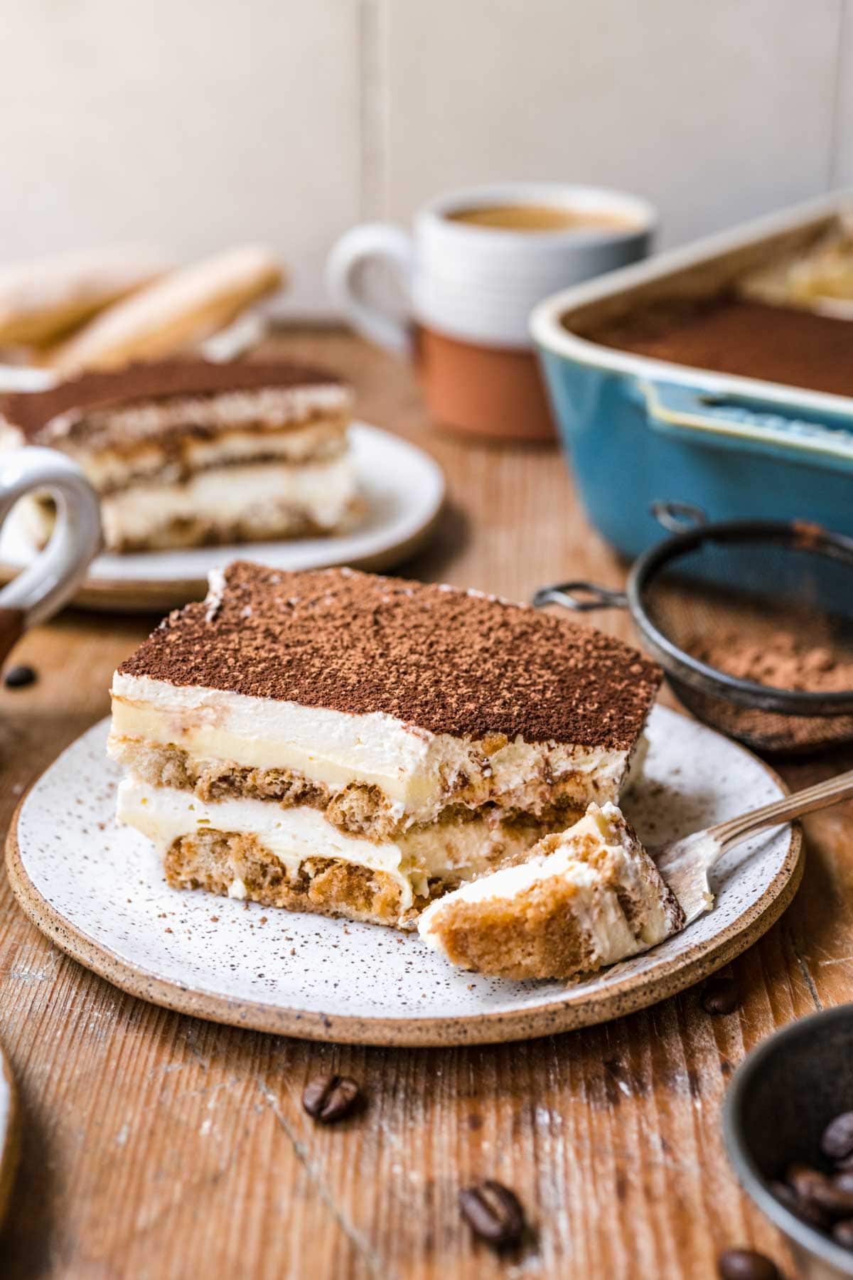 Tiramisu sliced on a white plate with a fork cutting a bite.