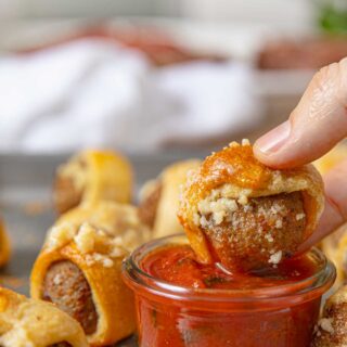 Garlic Bread Meatball Bites being dipped into a cup of Marinara Sauce with basil