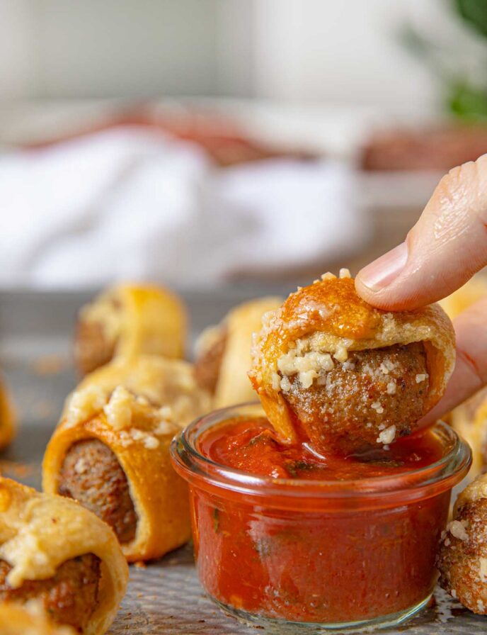 Garlic Bread Meatball Bites being dipped into a cup of Marinara Sauce with basil