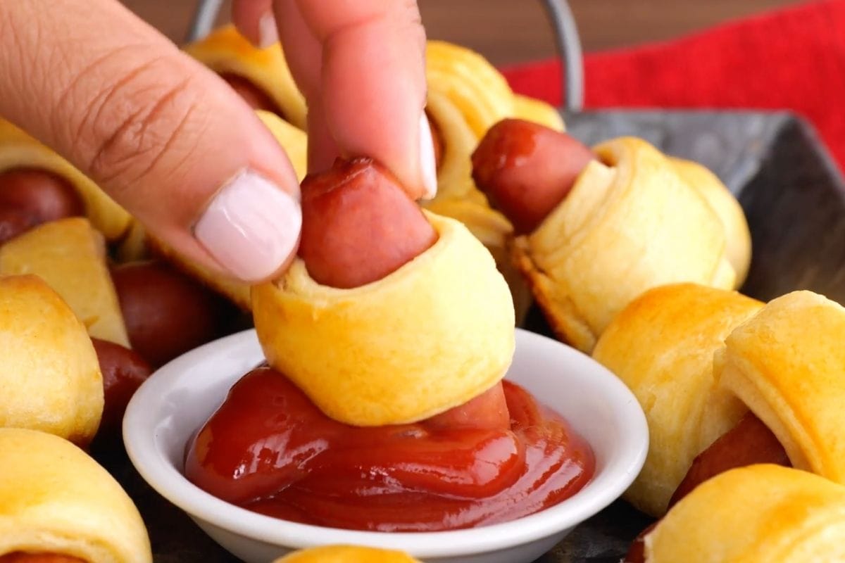 Pigs in a blanket being dipped in ketchup
