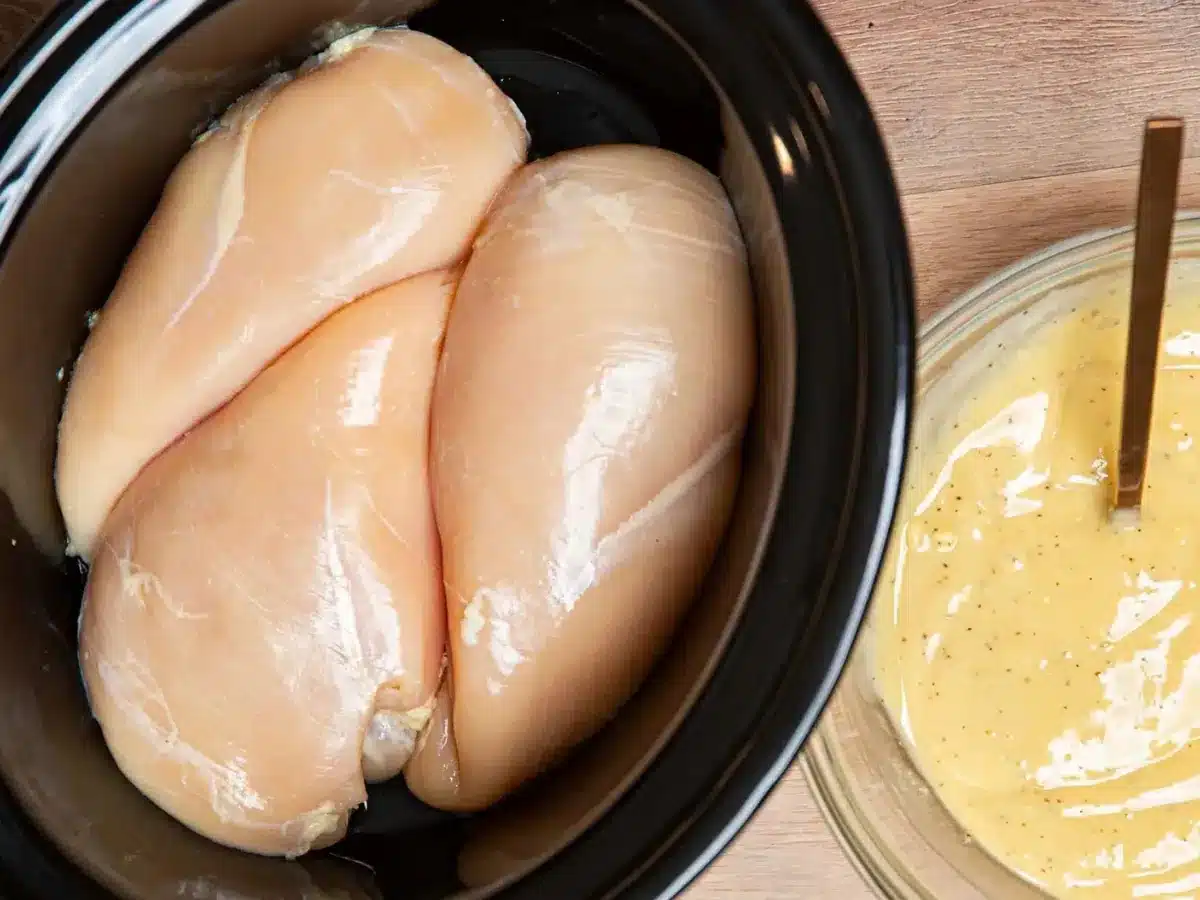 raw chicken in slow cooker with sauce in bowl
