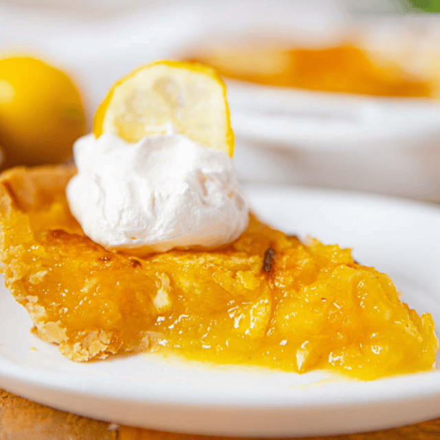 A slice of fruit pie with whipped cream and a lemon garnishment on a white plate