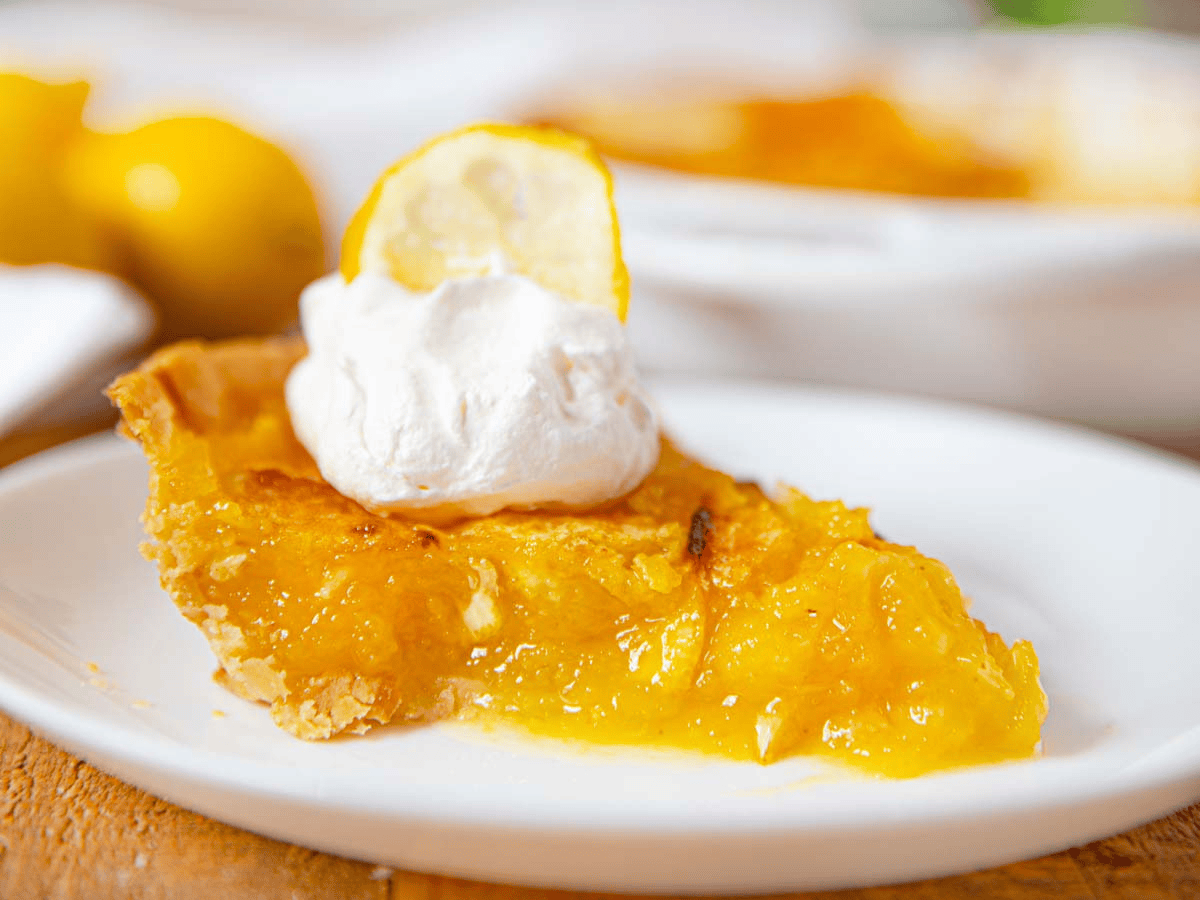 A slice of fruit pie with whipped cream and a lemon garnishment on a white plate