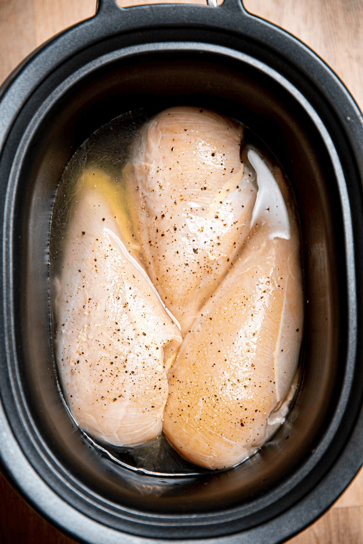 Raw chicken and chicken broth in a crockpot