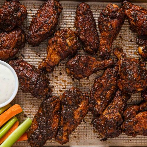Baked chicken wings on a baking sheet with sauce and veggies