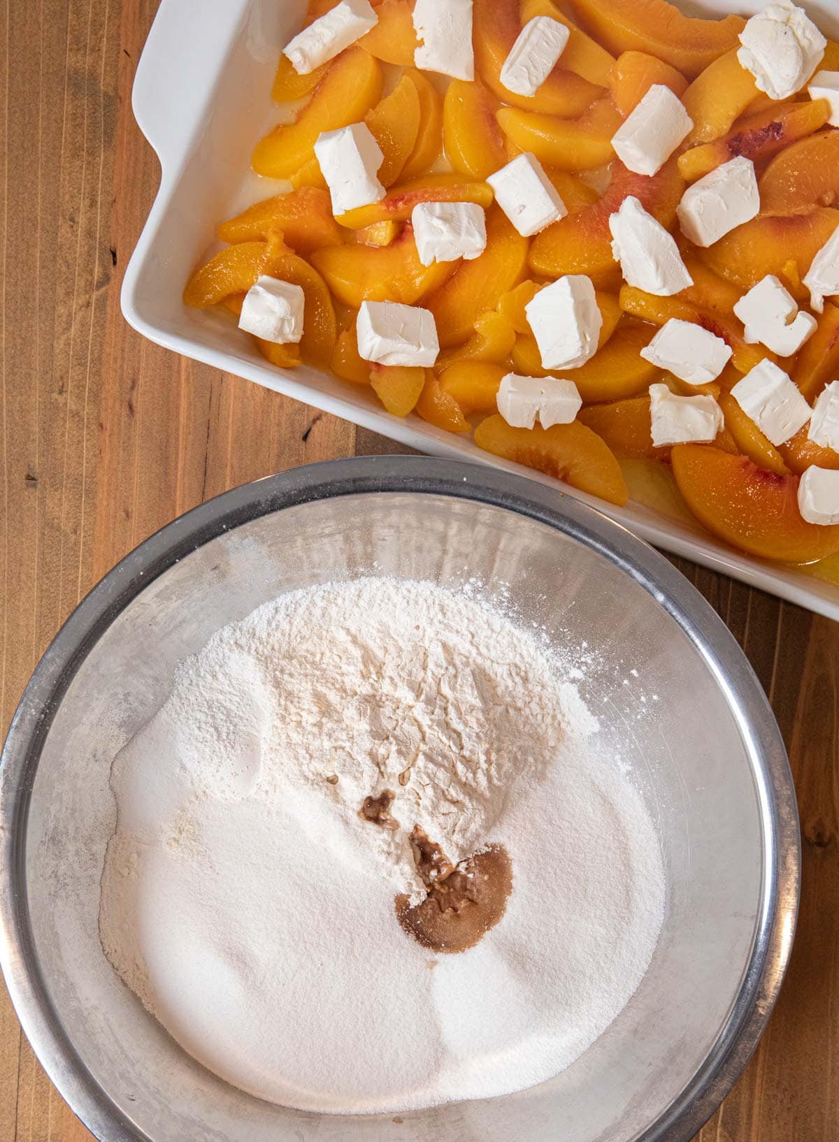 Peaches and Cream Cobbler dry ingredients in bowl with peaches and cream cheese in baking dish