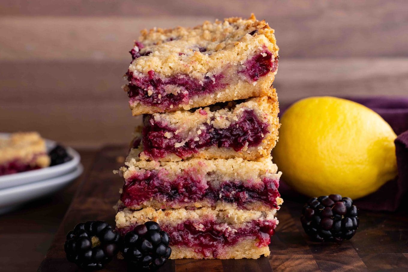 Blackberry Crumb Bars in a stack on cutting board with lemon and blackberries