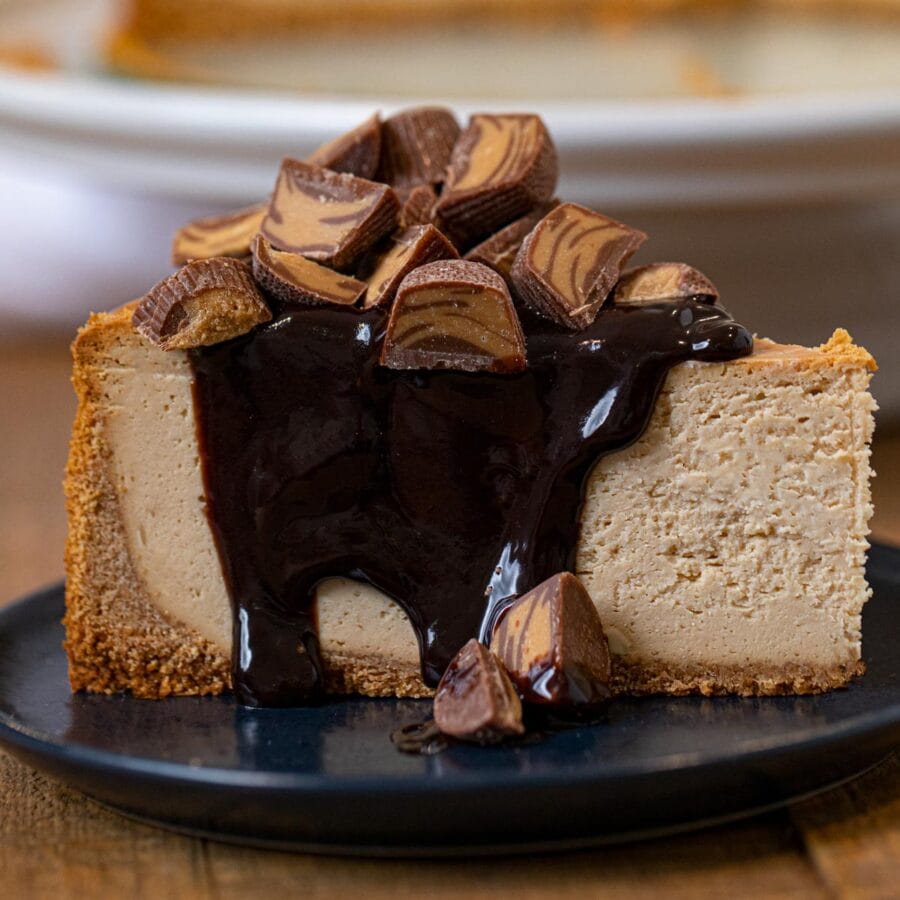Peanut Butter Cheesecake slice on plate with chocolate sauce and peanut butter cups
