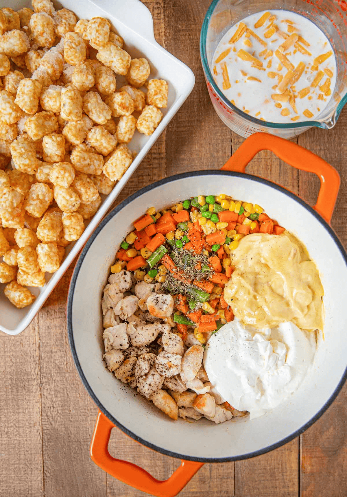 Casserole filling in a Dutch oven, tater tots on a baking dish, and cheese mixture in a measuring cup
