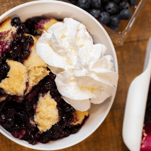 A scoop of fruit dessert in a bowl topped with whipped cream on a wood table