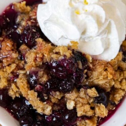 Crisp in a white bowl with whipped cream, ready to serve.