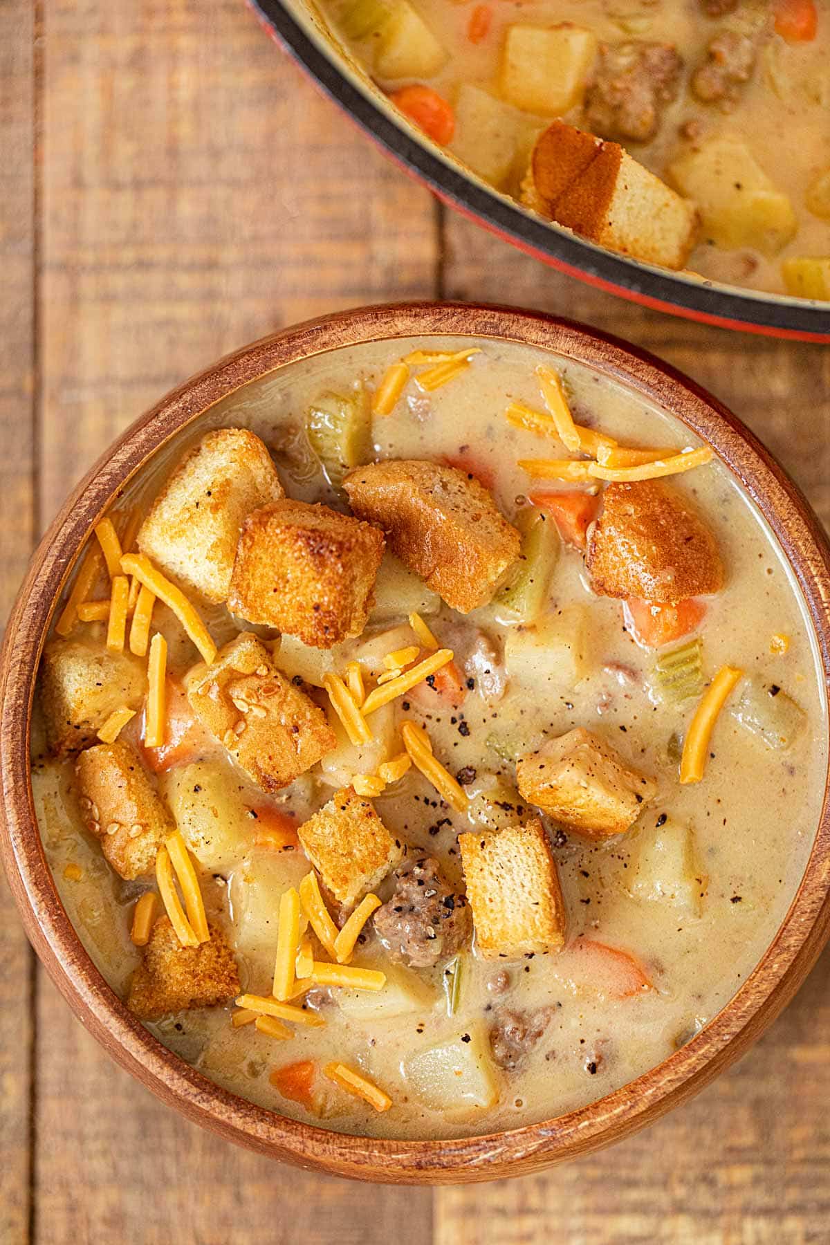 Cheeseburger Soup in wooden bowl with cheese and hamburger bun croutons