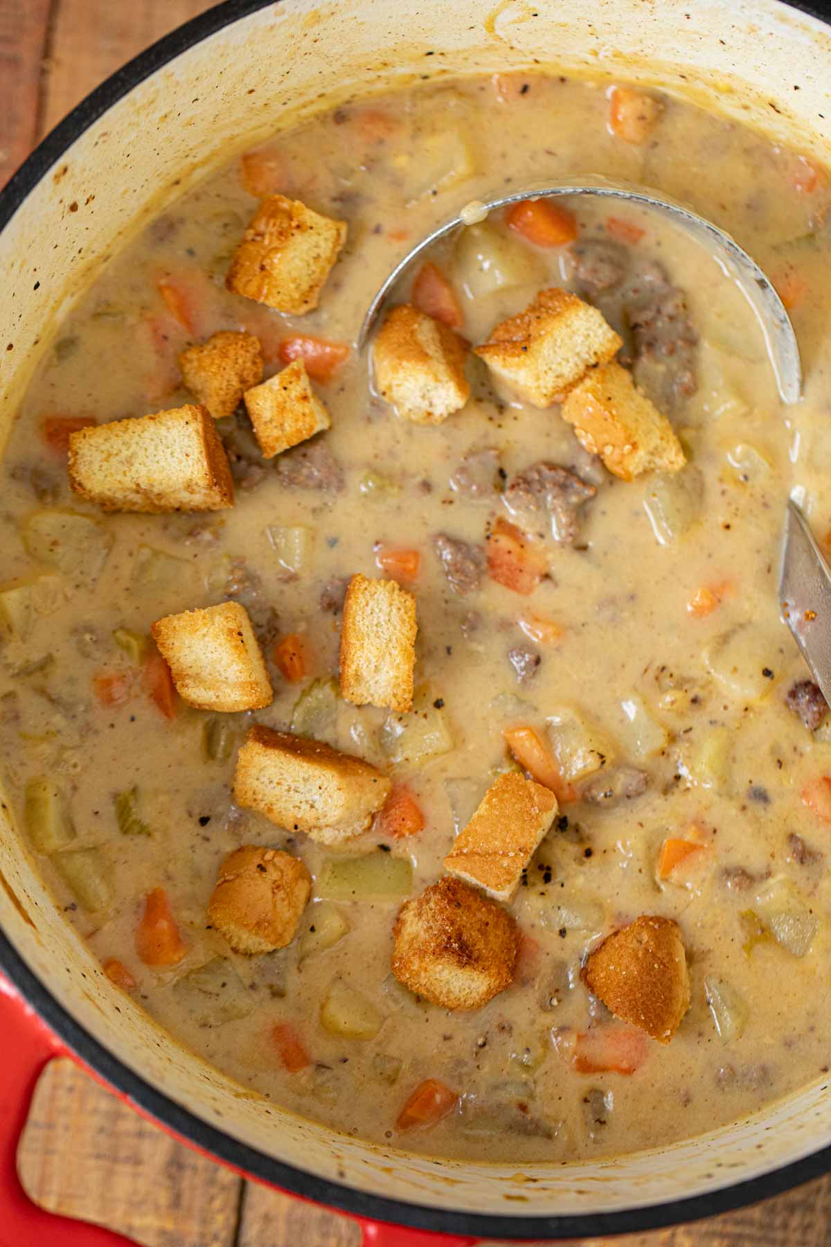 Cheeseburger Soup in pot with hamburger bun croutons and ladle