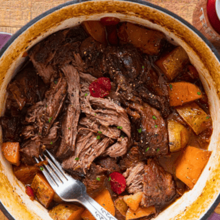 shredded beef in sauce with cherries and potatoes in a dutch oven with a fork