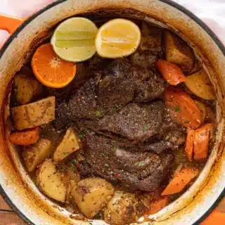 roast in pot with potatoes, carrots, lemon, lime, and orange slices