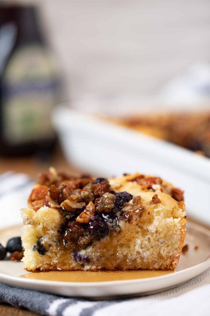 Slice of blueberry sausage pecan breakfast casserole on white plate with maple syrup