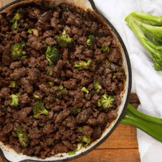 meat and broccoli in a green skillet with whole broccoli beside it