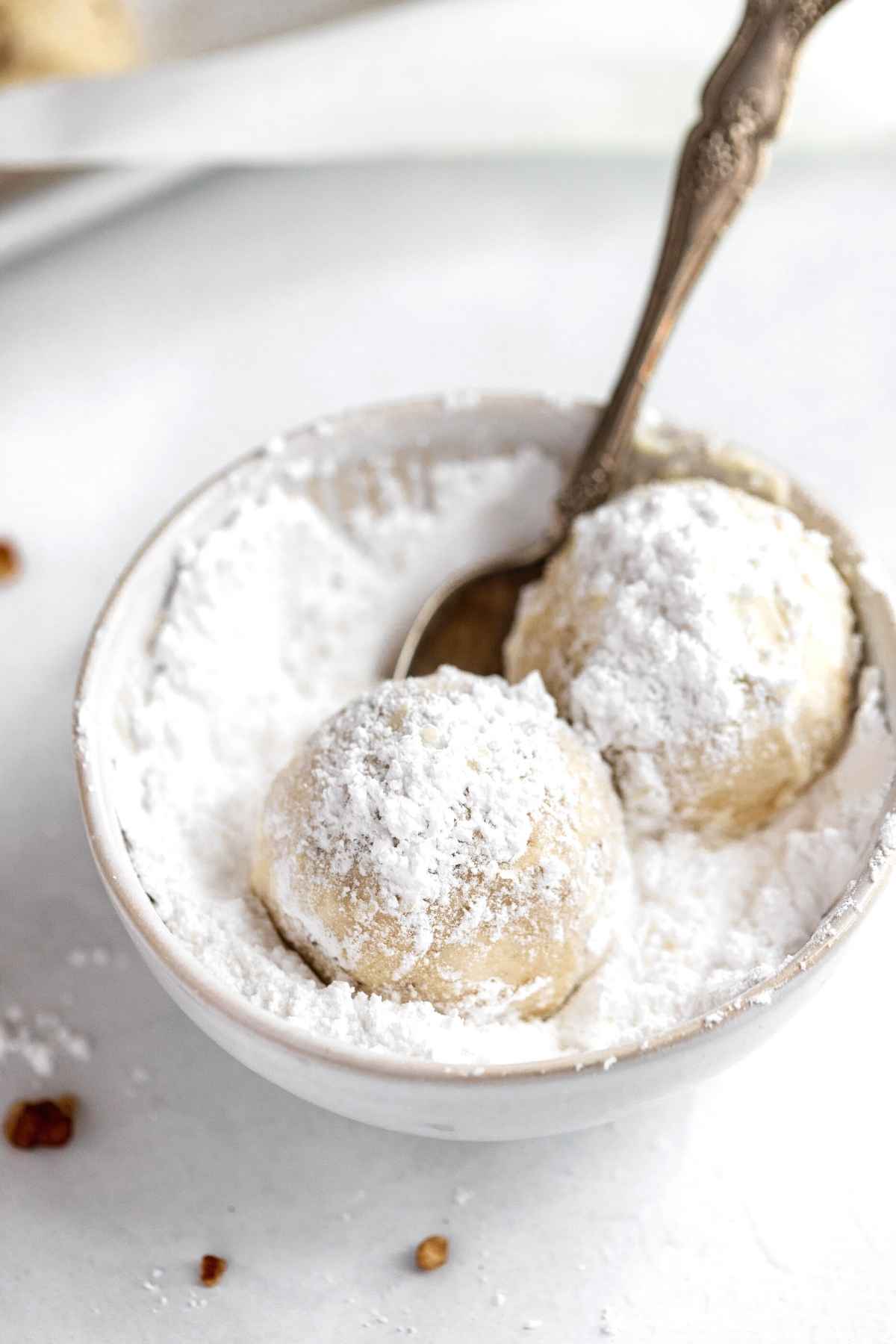 Snowball Cookies being rolled in powdered sugar in bowl with spoon