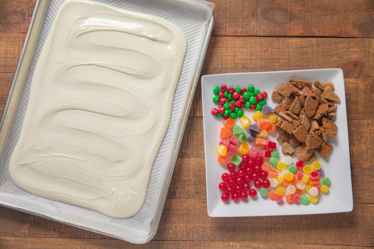 Gingerbread House Candy Bark poured chocolate on baking pan with candy topping on separate plate