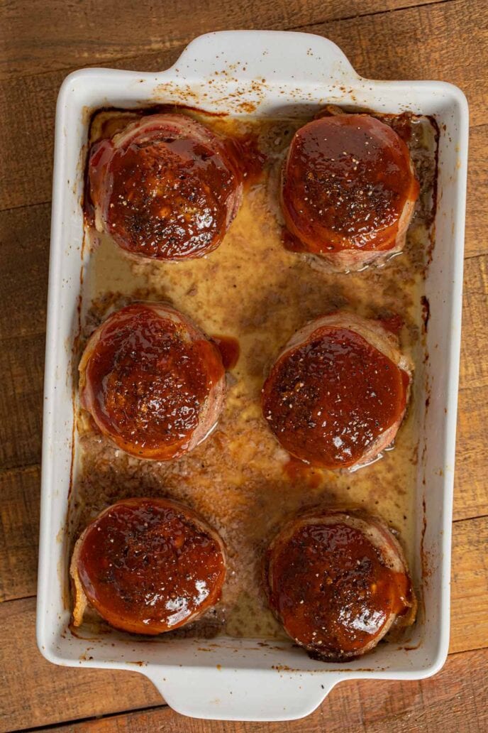 Individual Bacon Wrapped Meatloaf in baking dish with ketchup glaze