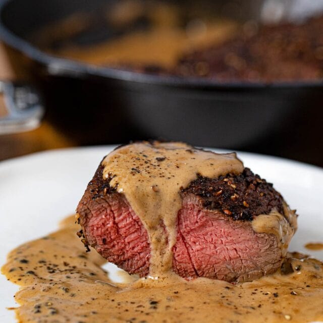 Steak Au Poivre sliced open on plate with pepper sauce