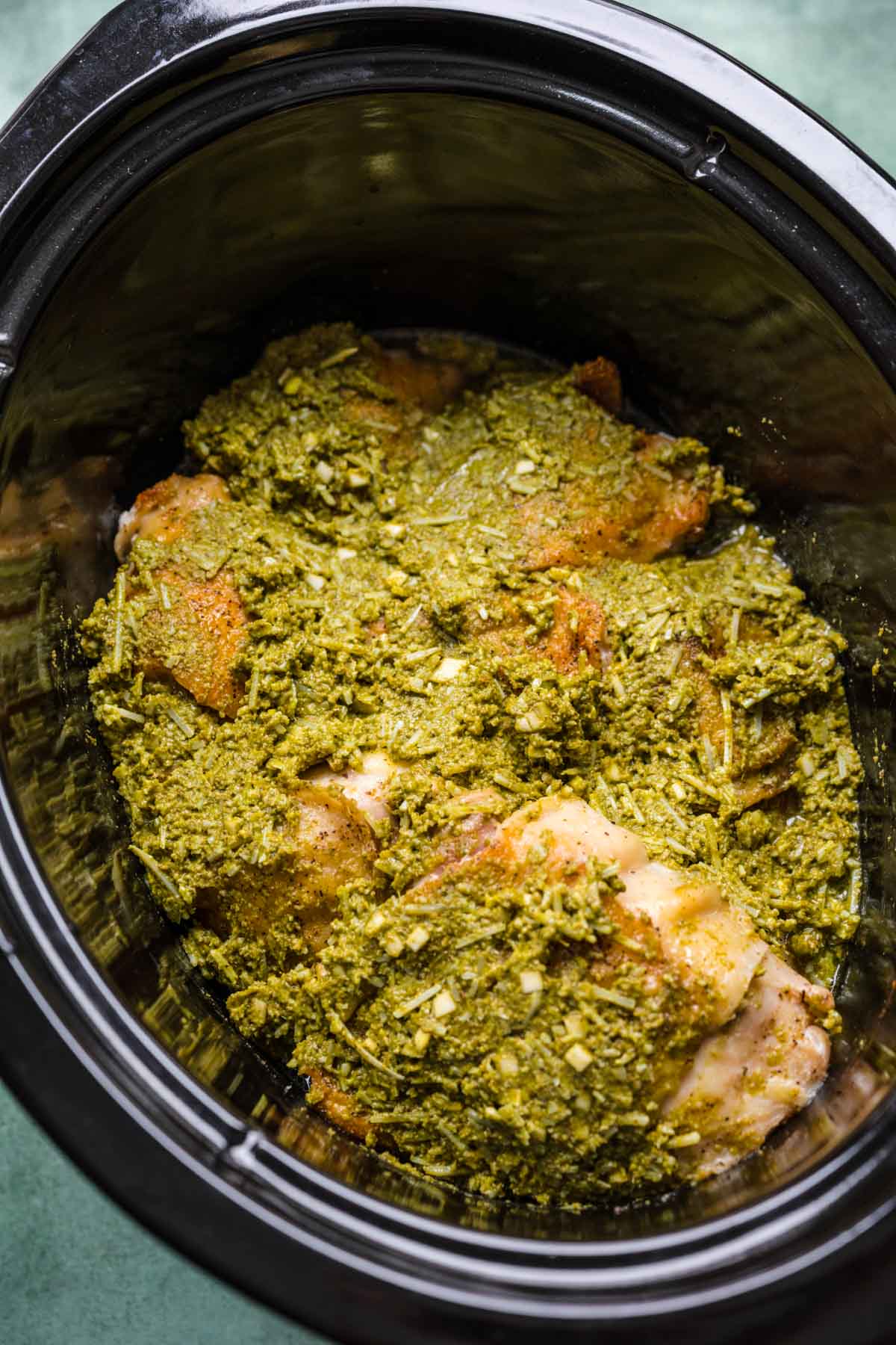 Slow Cooker Pesto Chicken in bottom of slow cooker with pesto sauce