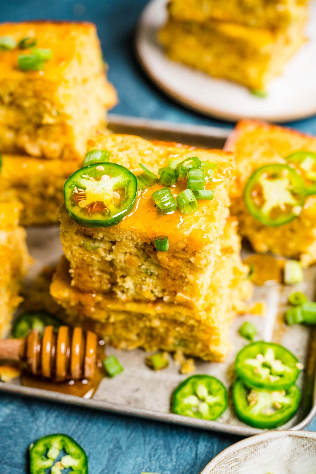 Spicy Mexican Cornbread squares stacked on serving plate with jalapeno slices and honey drizzled