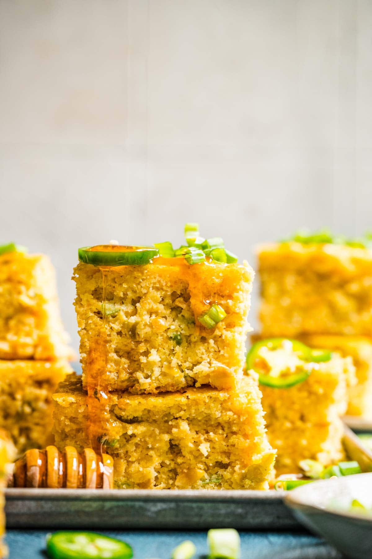 Spicy Mexican Cornbread squares stacked on serving plate with jalapeno slices and honey drizzled