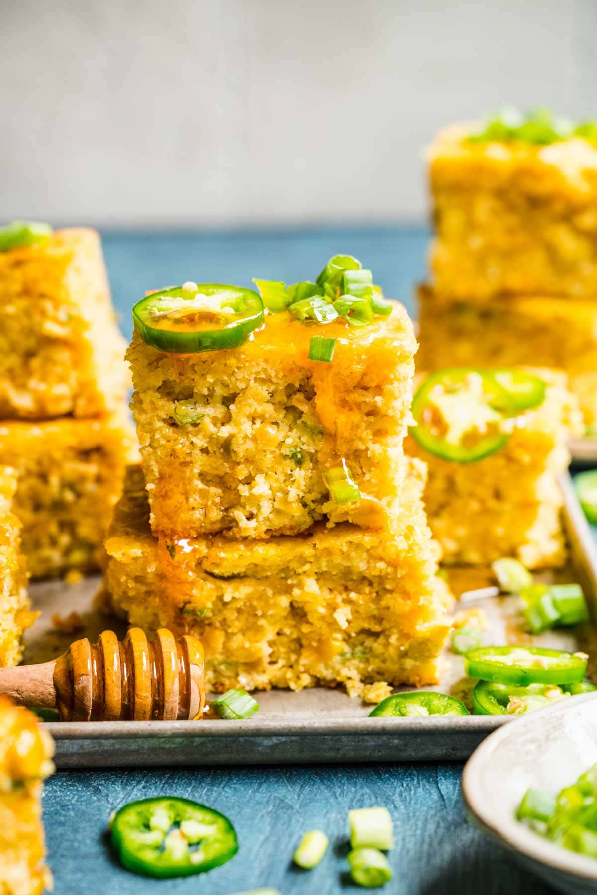 Spicy Mexican Cornbread squares stacked on serving plate with jalapeno slices and honey drizzled