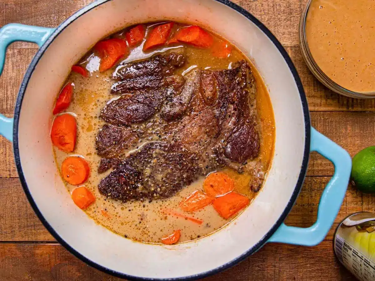 beef covered in sauce with carrots in pot