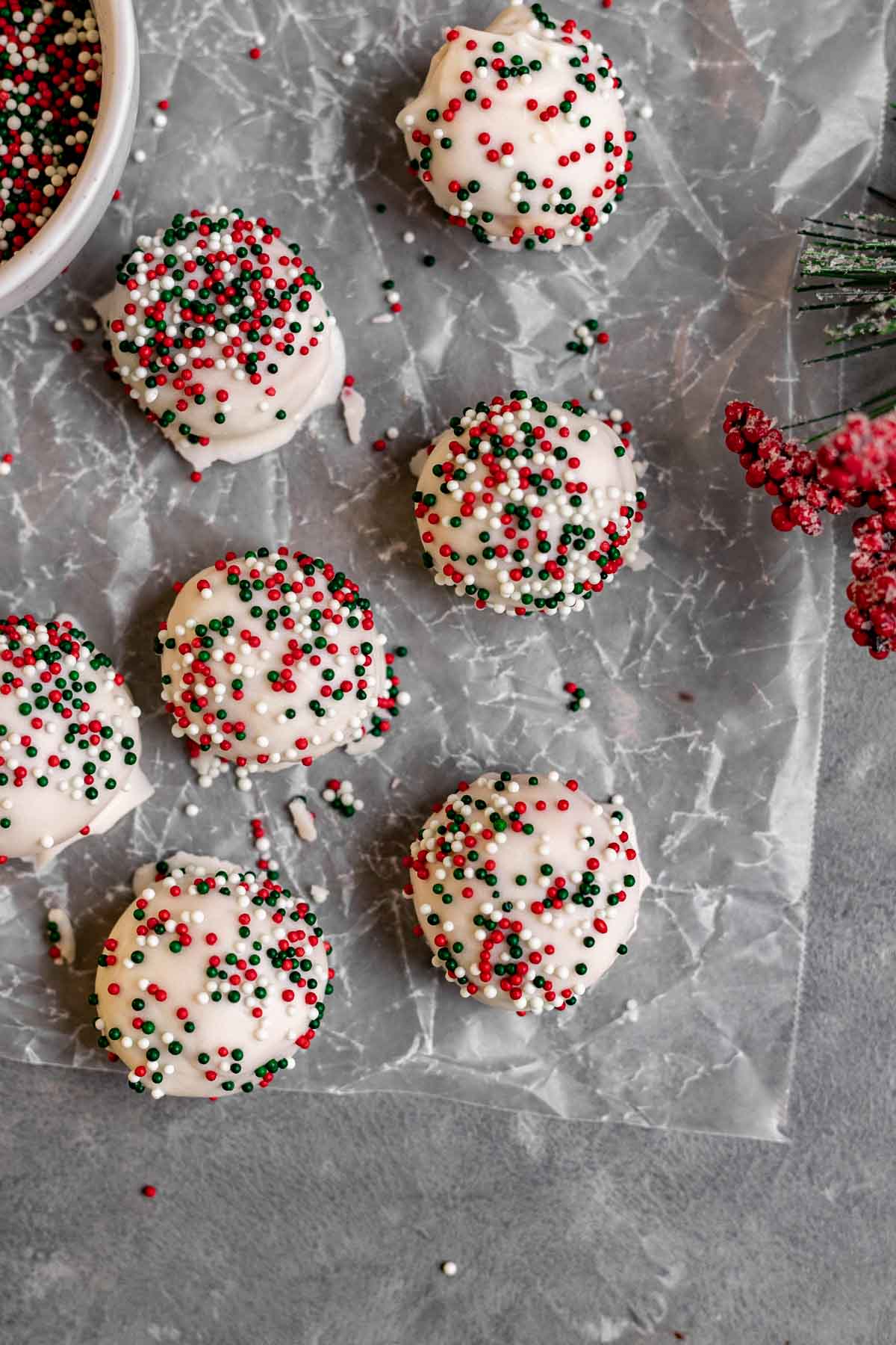 Peanut Butter Snowballs covered in white chocolate and holiday sprinkles on parchment