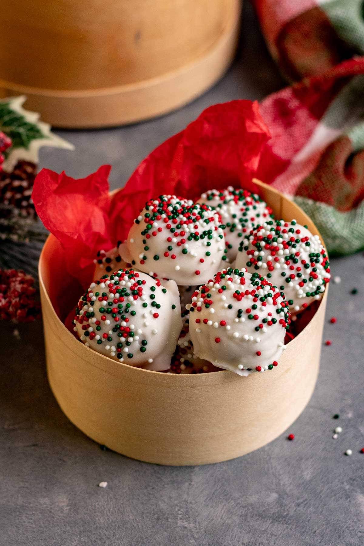 Peanut Butter Snowballs covered in white chocolate and holiday sprinkles in a gift box