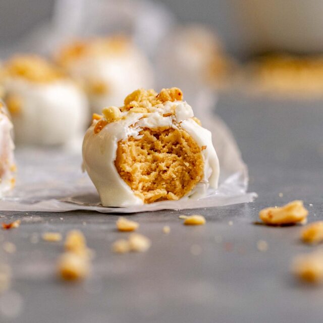 Peanut Butter Snowballs covered in white chocolate and crushed peanuts on parchment with bite taken