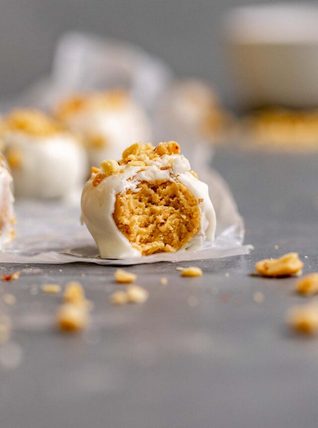 Peanut Butter Snowballs covered in white chocolate and crushed peanuts on parchment with bite taken