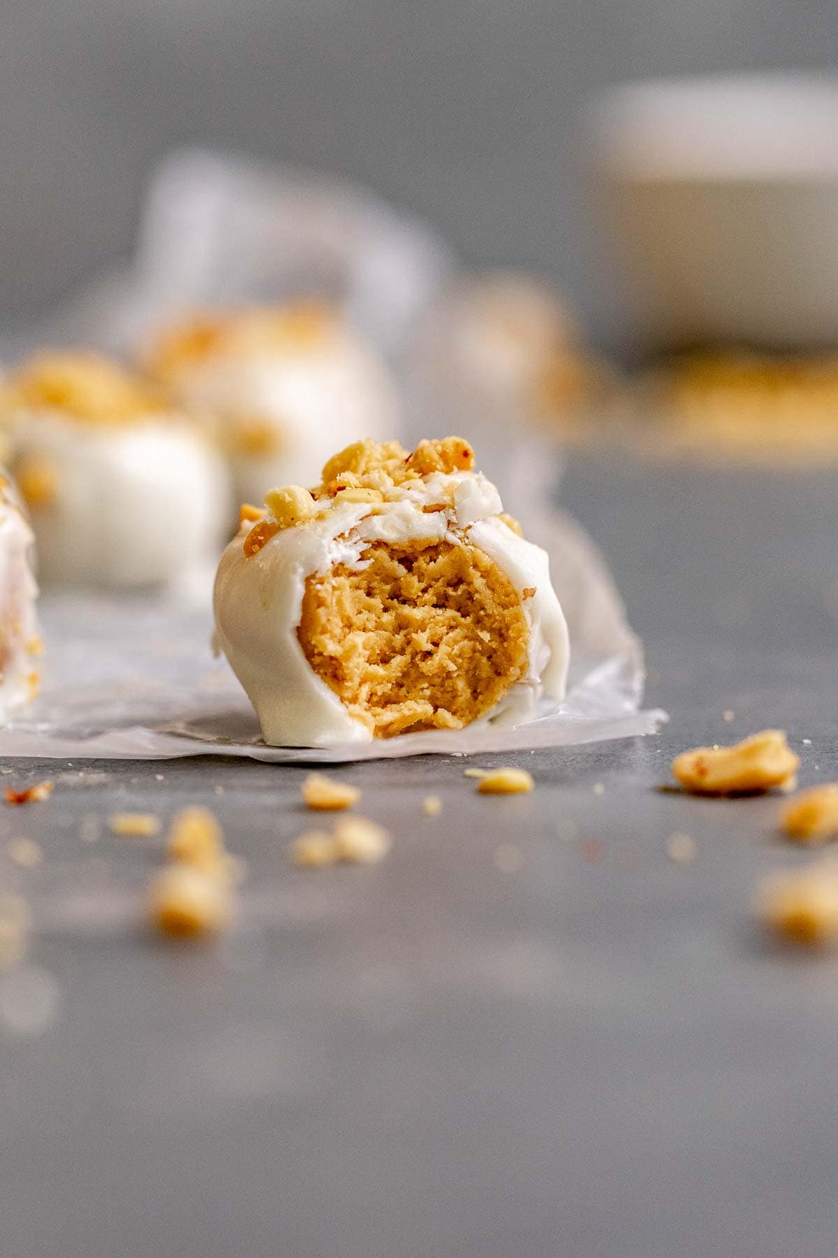 Peanut Butter Snowballs covered in white chocolate and crushed peanuts on parchment with bite taken
