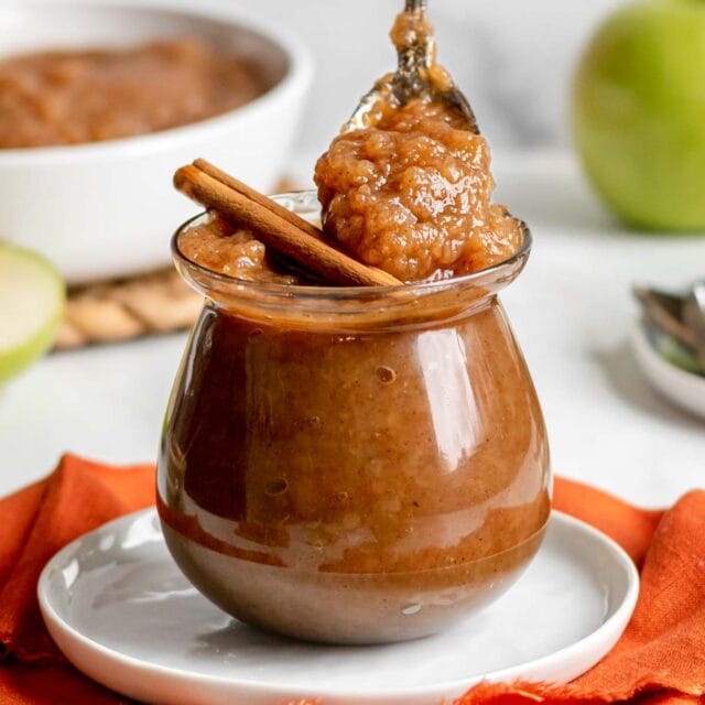 Slow Cooker Applesauce in jar with cinnamon stick and spoon
