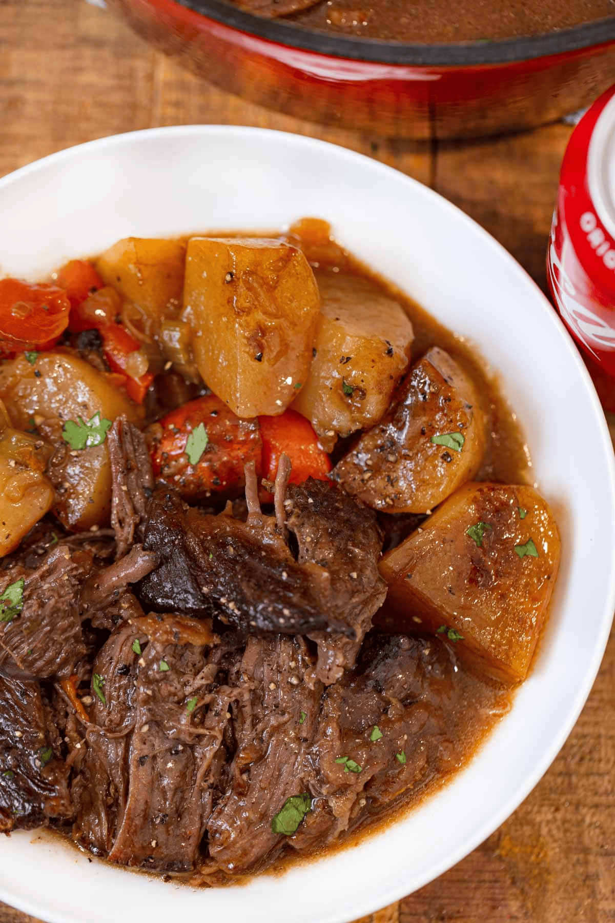 White bowl of pot roast with partially visible can of coke