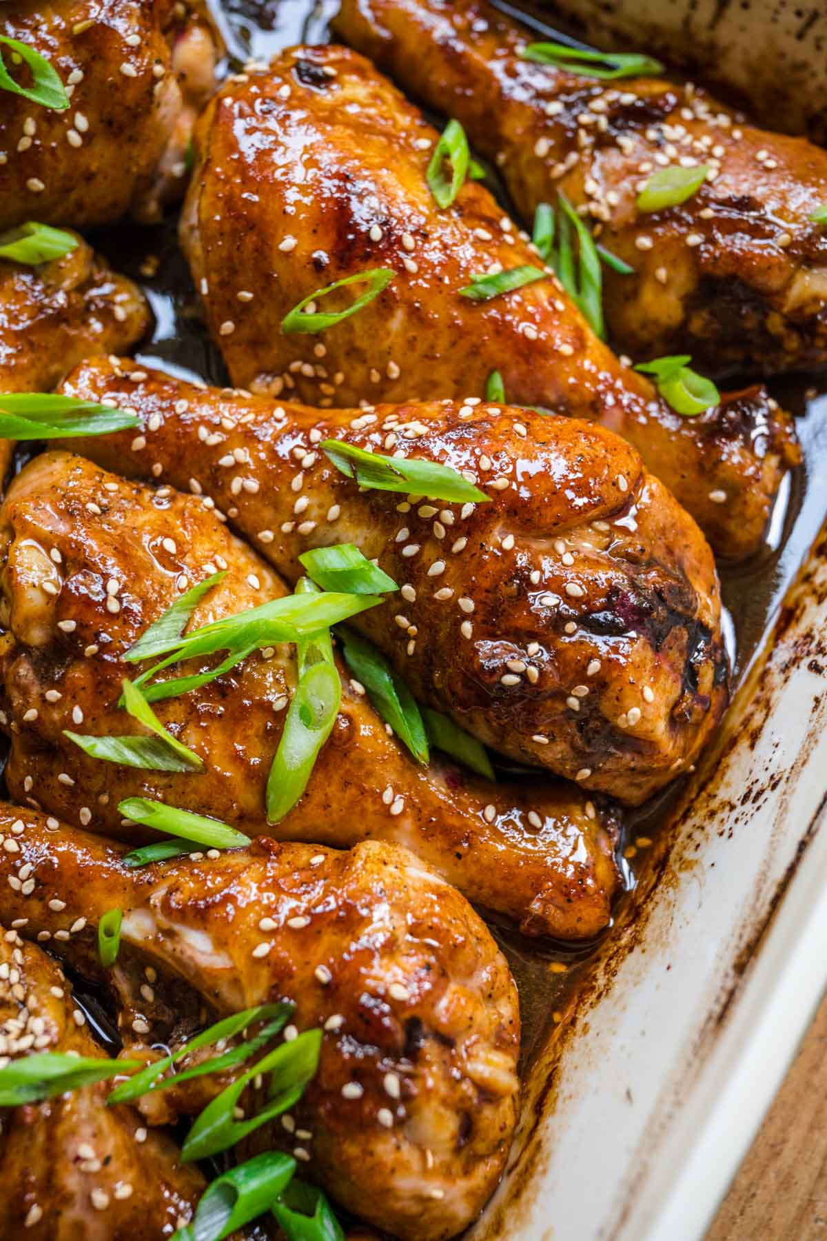 Brown Sugar Garlic Baked Chicken Legs sauce and chicken in baking dish with sliced green onions and sesame seeds