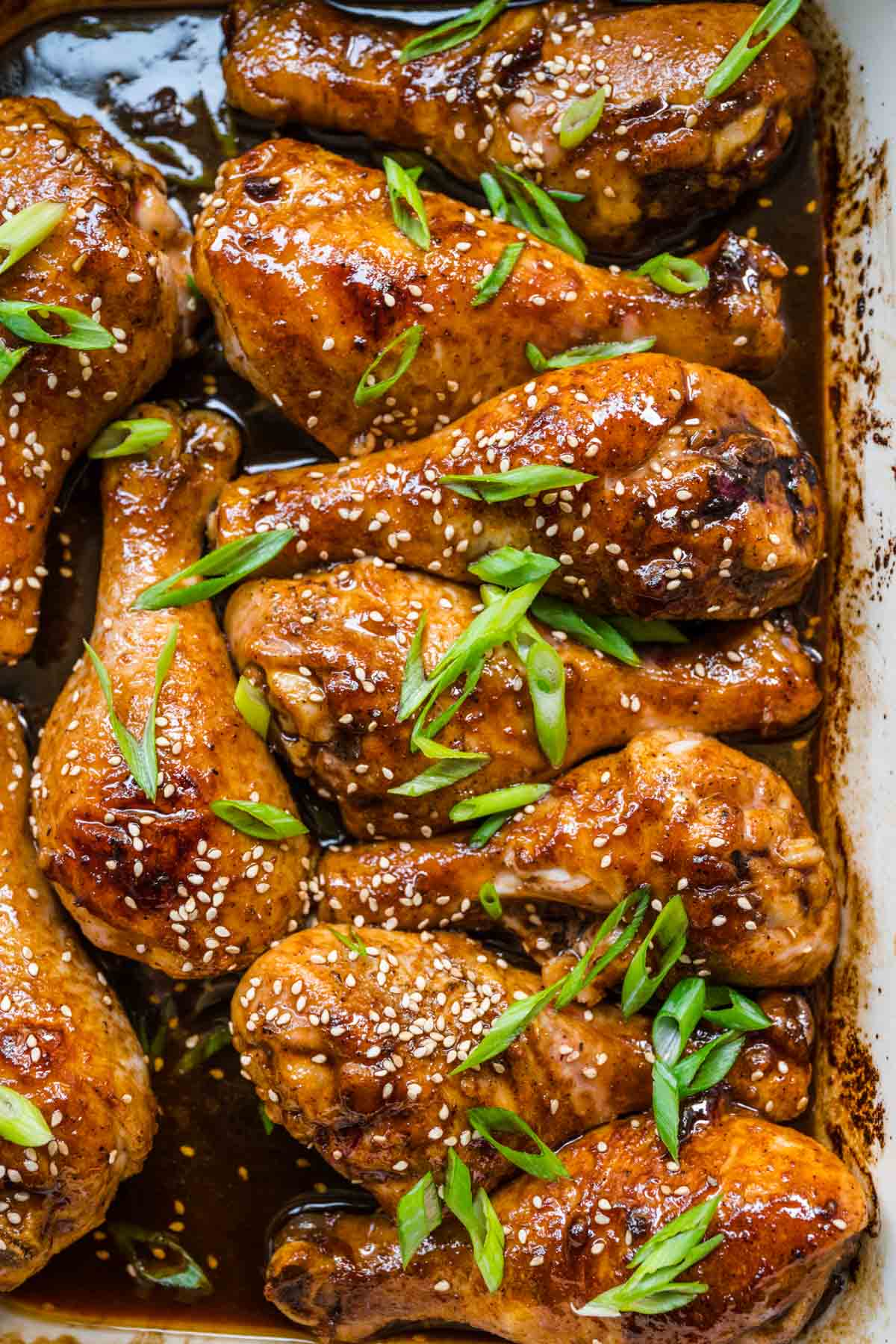 Brown Sugar Garlic Baked Chicken Legs sauce and chicken in baking dish with sliced green onions and sesame seeds