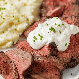 sauce topped on steak with mashed potatoes on the side.